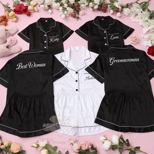 May include: Black and white satin pajama sets with white piping. The sets include a button-down top and shorts. Text on the pajamas includes "Kaky", "Luna", "Best Woman", "Groomswoman", and "Audrie".