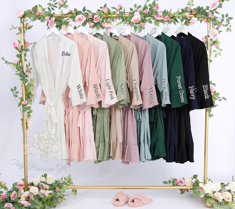 Puede incluir: Una exhibici&oacute;n de batas de varios colores colgadas en un estante dorado, incluyendo blanco, rubor, rosa claro, salvia, champ&aacute;n, malva, azul polvoriento, verde bosque, azul marino y negro. Cada bata tiene un cintur&oacute;n a juego y est&aacute; etiquetada con su nombre de color.