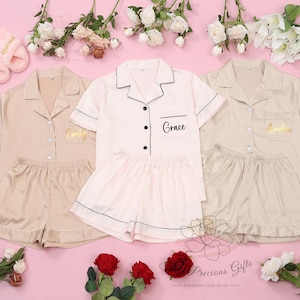 Puede incluir: Tres conjuntos de pijamas a juego en beige, blanco y rosa con mangas cortas y pantalones cortos. Cada conjunto tiene un nombre personalizado en el bolsillo: Emily, Grace y Amelia.