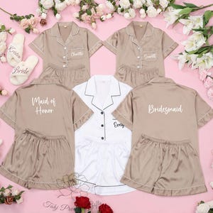 Puede incluir: Cuatro conjuntos de pijamas a juego en color marr&oacute;n claro con ribetes blancos. Las pijamas tienen mangas cortas y pantalones cortos. Cada conjunto tiene un t&iacute;tulo diferente bordado en la espalda: "Bride", "Maid of Honor", "Bridesmaid" y "Evelyn".