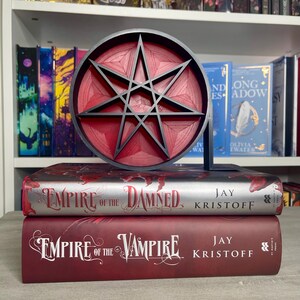 May include: Two hardcover books, "Empire of the Damned" and "Empire of the Vampire" by Jay Kristoff, with a red and black eight-pointed star bookend.