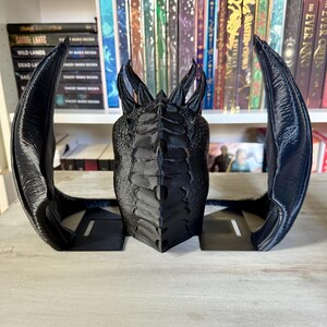 May include: Black dragon bookends with a detailed, textured design. The dragon's wings are spread out and the head is facing forward. The bookends are made of a durable material and are perfect for holding books or other items.