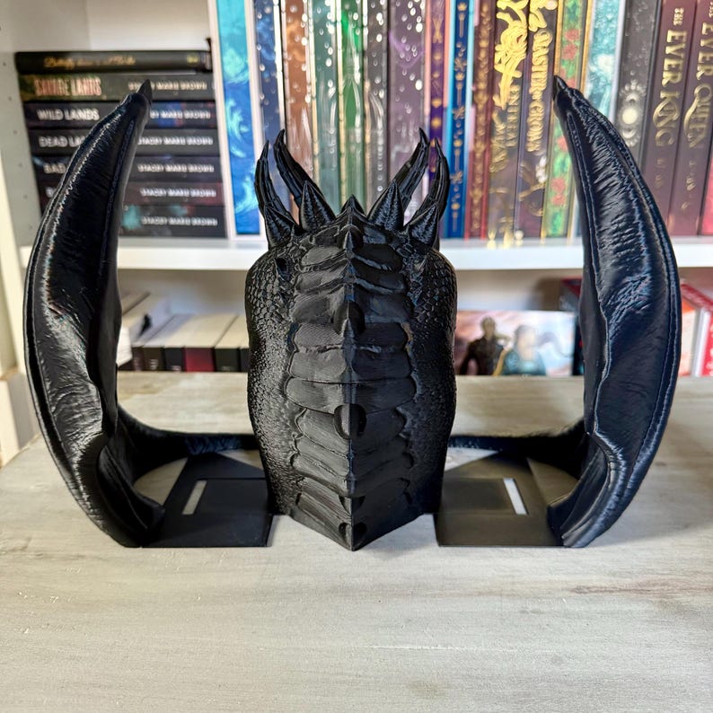 May include: Black dragon bookends with a detailed, textured design. The dragon's wings are spread out and the head is facing forward. The bookends are made of a durable material and are perfect for holding books or other items.