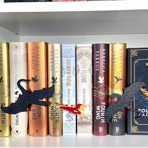 May include: A bookshelf with a set of fantasy novels by Rebecca Yarros. The books are titled "Iron Flame", "Fourth Wing", "Iron Wing", "Fourth Wing", "Iron Wing", "Fourth Wing", "Iron Wing", and "Fourth Wing". The books are arranged in order of publication date. A black dragon bookend is holding up the books.