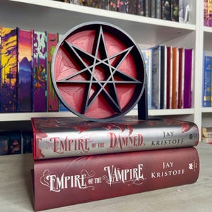May include: Two hardcover books titled "Empire of the Damned" and "Empire of the Vampire" by Jay Kristoff. A black and red eight-pointed star bookend is on top of the books.