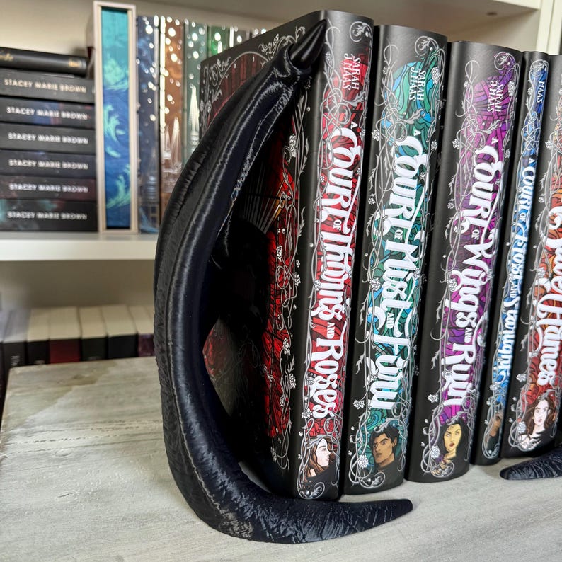 May include: A set of five fantasy novels with black covers and silver lettering. The titles are "A Court of Thorns and Roses", "A Court of Mist and Fury", "A Court of Wings and Ruin", "A Court of Frost and Starlight", and "A Court of Silver Flames".