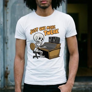 Może przedstawiać: Biały t-shirt z krótkim rękawem z grafiką przedstawiającą szkielet siedzący przy konsoli mikserskiej z głośnikami. Napis nad grafiką brzmi "JUST ONE MORE TWEAK" pomarańczowymi literami i jest umieszczony centralnie na klatce piersiowej.