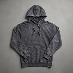 May include: A charcoal gray hoodie with a drawstring hood and a kangaroo pocket. The sweatshirt has a faded, textured appearance. The garment is laid flat on a gray surface.