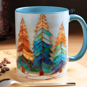 May include: A ceramic mug with a light blue interior and handle. The exterior features a design of three stylized evergreen trees in shades of orange, blue, and green. The mug is set on a wooden surface with a spoon and a pastry.