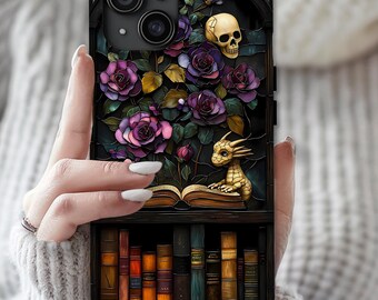 May include: A phone case featuring a dark, stained-glass style illustration of purple roses, a human skull, and a small golden dragon perched on an open book. Below the book, a shelf displays a row of various colorful, vintage-style hardcover books.
