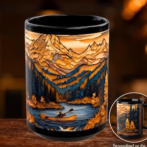 May include: A black ceramic mug featuring a wrap-around graphic of a person paddling a yellow canoe on a lake, surrounded by dark blue pine trees and tall, jagged orange-toned mountains under a sunset sky. The text reads Your Name Here.