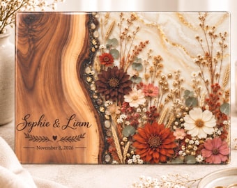 Könnte beinhalten: Eine rechteckige Holzplatte mit natürlicher Maserung auf der linken Seite und einer mit Harz gefüllten rechten Seite, die mit getrockneten Blumen in Rot, Weiß und Rosa verziert ist. Der Text lautet Sophie & Liam und November 8, 2026.