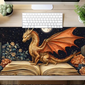 May include: A gold dragon with orange wings perched on an open book with a dark blue background and a full moon. The book is surrounded by flowers and stars.