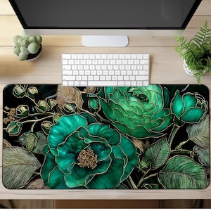 May include: A large, rectangular mousepad featuring a detailed floral design. The design showcases large, teal-green flowers with gold outlines and accents against a black background. The mousepad is placed on a light wood desk, with a keyboard and monitor visible.