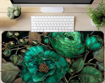 May include: A large, rectangular mousepad featuring a detailed floral design. The design showcases large, teal-green flowers with gold outlines and accents against a black background. The mousepad is placed on a light wood desk, with a keyboard and monitor visible.