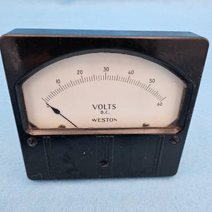 May include: A black Weston DC voltmeter with a white face and black needle. The gauge reads up to 60 volts, with markings at 10, 20, 30, 40, 50, and 60. The text "VOLTS D.C. WESTON" is printed on the face.