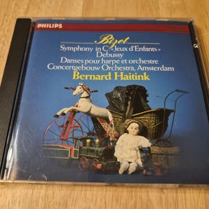 May include: A CD case featuring a blue cover with the text "Bizet Symphony in C Jeux d'Enfants Debussy Danses pour harpe et orchestre". The cover art depicts a toy train, a horse-drawn carriage, and a doll.