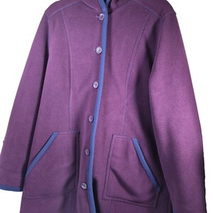 May include: A purple fleece hooded jacket featuring a button-down front closure, long sleeves, and two front patch pockets. The garment is accented with contrasting blue trim along the hood, the button placket, the pocket edges, and the hemline.