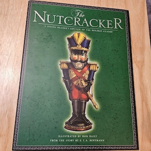 May include: The Nutcracker book cover. The cover features a detailed illustration of a toy soldier in a blue and gold uniform. The title is in white, with the text "A Young Reader's Edition of the Holiday Classic" below. Illustrated by Don Daily.