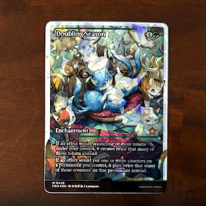 May include: A Magic: The Gathering card with a holographic finish. The card is titled "Doubling Season" and is an enchantment. The card art features a group of cats in a variety of colors and patterns.
