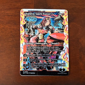 May include: A trading card featuring Chandra, Spark Hunter, a legendary planeswalker from the Magic: The Gathering card game. The card is illustrated with Chandra riding a red vehicle with a fiery background. The card text describes Chandra's abilities, including creating a vehicle artifact token and dealing damage to any target.