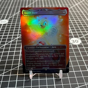 May include: A holographic trading card featuring a white character with blue eyes and red shoes, titled "Super State." The card has a red and orange background with the text "Legendary Enchantment - Aura."