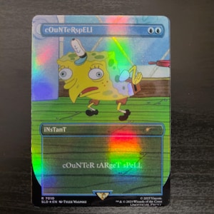 May include: A Magic: The Gathering card with a blue, green, and yellow background. The card features a cartoon image of Spongebob Squarepants with the text "cOuNTeRspELL" and "iNsTanT" on the card.