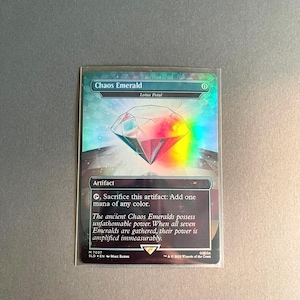 May include: A holographic trading card titled "Chaos Emerald" featuring a gem design with red and blue hues. The card includes text about its artifact status and ability to add mana. The card is in a protective sleeve.
