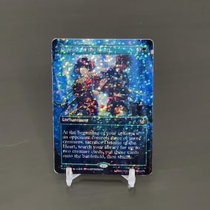 May include: A holographic trading card titled "Defense of the Heart" with a shimmering blue background. The card features two figures and includes game text. The card is displayed on a clear plastic stand.