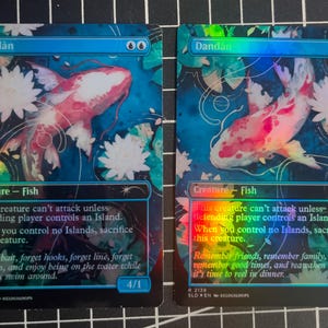 May include: Two trading cards featuring a vibrant koi fish design. The fish is depicted in shades of pink and white, swimming among white flowers and blue water. The card text reads "Dandan" and "Creature - Fish".