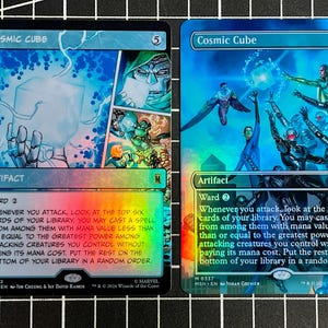 May include: Two rectangular trading cards titled Cosmic Cube, each featuring a holographic finish and Marvel character illustrations. The cards display game text, a mana cost of 5, and the artifact type. Both cards show the same rules text.