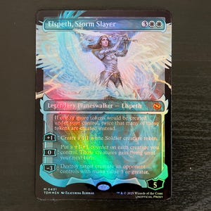 May include: A Magic: The Gathering card featuring Elspeth, Storm Slayer. The card is a legendary planeswalker with a blue, white, and red background. The card text reads: "If one or more tokens would be created under your control, twice that many of those tokens are created instead. +1: Create a 1/1 white Soldier creature token. 0: Put a +1/+1 counter on each creature you control. Those creatures gain flying until your next turn. -3: Destroy target creature an opponent controls with mana value 3 or greater."