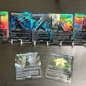 May include: A collection of Magic: The Gathering trading cards, featuring various artwork and card types. The cards are displayed on clear stands, showcasing their holographic foil designs and detailed illustrations. The cards include "Clive's Invictus Blade" and "Gai's Dark Hammer."