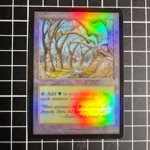 May include: A holographic trading card titled "Gaea's Cradle." The card features a fantasy landscape with trees and text. The text includes the card's name, rules, and flavor text. The card is on a black and white grid.