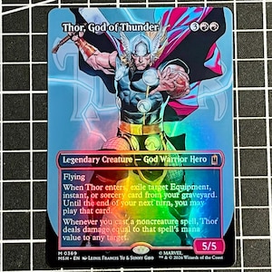 May include: A holographic trading card featuring Thor, God of Thunder, depicted with a winged helmet, cape, and hammer. The card text includes 'Legendary Creature - God Warrior Hero', 'Flying', and game mechanics, with a 5/5 power and toughness rating.