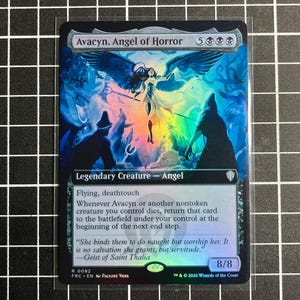 May include: A holographic Magic: The Gathering trading card titled Avacyn, Angel of Horror. The card features a central winged figure in white robes, surrounded by dark silhouettes, with text detailing the creature's abilities, power, and toughness.