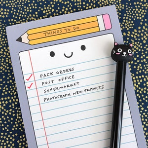 May include: A gray notepad with a checklist and the text "Things to do" at the top. The notepad has a cartoon face with a pencil and a black cat pen.