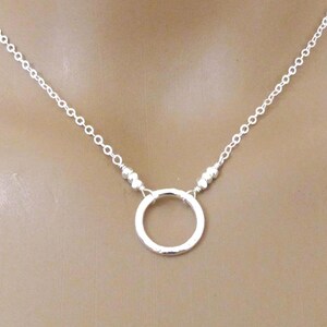 May include: A delicate silver necklace featuring a small, open circle pendant. The pendant is suspended from a fine chain with small beads on either side of the circle. The necklace is shown against a neutral background.