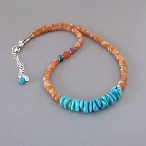May include: A beaded necklace featuring faceted orange sunstone beads, a section of bright turquoise nuggets, and small accent beads in teal, orange, and magenta. The necklace includes a silver-toned metal chain extender with a small turquoise bead.