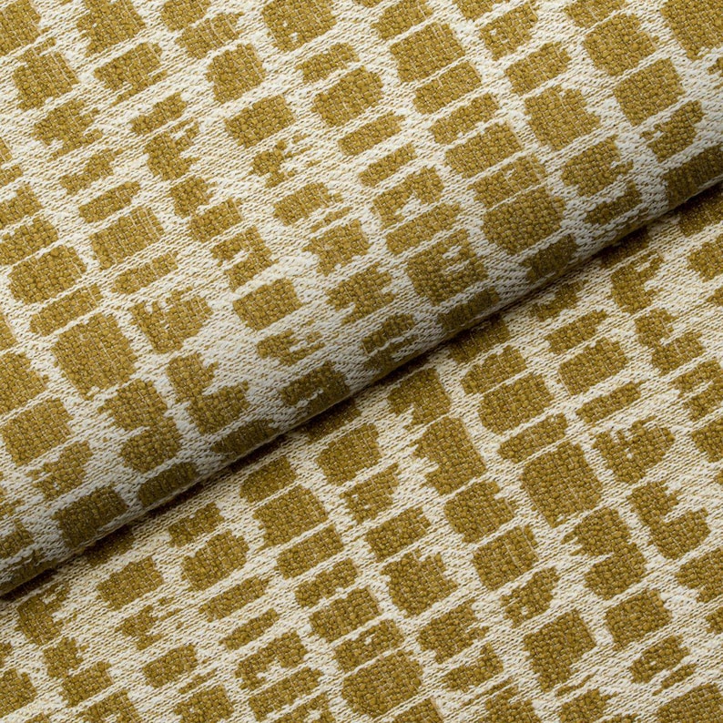 K&ouml;nnte beinhalten: Nahaufnahme eines strukturierten Stoffes mit einem sich wiederholenden Muster aus senffarbenen rechteckigen Formen auf cremefarbenem Hintergrund. Der Stoff ist gefaltet und zeigt seine Textur und sein Design. Das Muster erzeugt ein geometrisches, abstraktes Design.