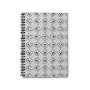 Peut inclure: Un carnet à reliure spirale présentant un motif répétitif noir et blanc de crânes et d'os croisés pixelisés disposés en grille. La couverture a un fond texturé gris clair avec une reliure à spirale noire sur le côté gauche.