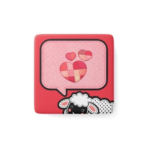 May include: A red square-shaped item with a speech bubble design. The bubble contains three hearts and a patchwork heart design. A cartoon sheep is at the bottom. The item is likely a case or cover.