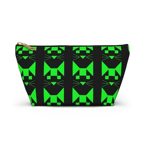 Op de afbeelding: Een zwart etui met ritssluiting voorzien van een herhalend geometrisch patroon van fel neongroene kattengezichten. Het ontwerp bestaat uit gestileerde driehoekige oren, vierkante ogen en eenvoudige lijnen als snorharen in een raster.