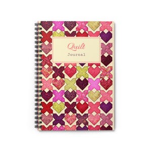 May include: Spiral-bound journal with a colorful quilt pattern cover. The cover features a patchwork design of hearts and X shapes in shades of red, pink, purple, and green. The journal has the words "Quilt Journal" printed on the cover.