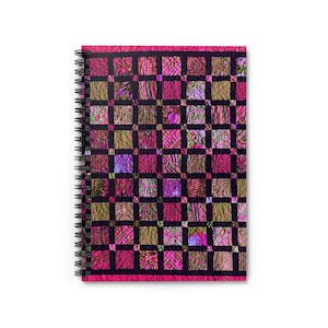 May include: A spiral-bound notebook with a vibrant, quilted pattern cover. The design features a grid of squares in shades of pink, purple, and olive green, set against a black background. The notebook's edges are trimmed in a solid pink.