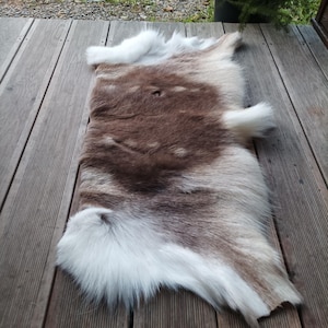 May include: A rectangular animal hide rug featuring a thick, soft coat with a blend of natural brown and white fur. The centre displays a deep brown coloration that transitions into long, fluffy white fur along the edges and corners.