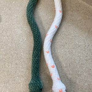May include: Two crocheted snake toys. One is green and the other is white with pink hearts.