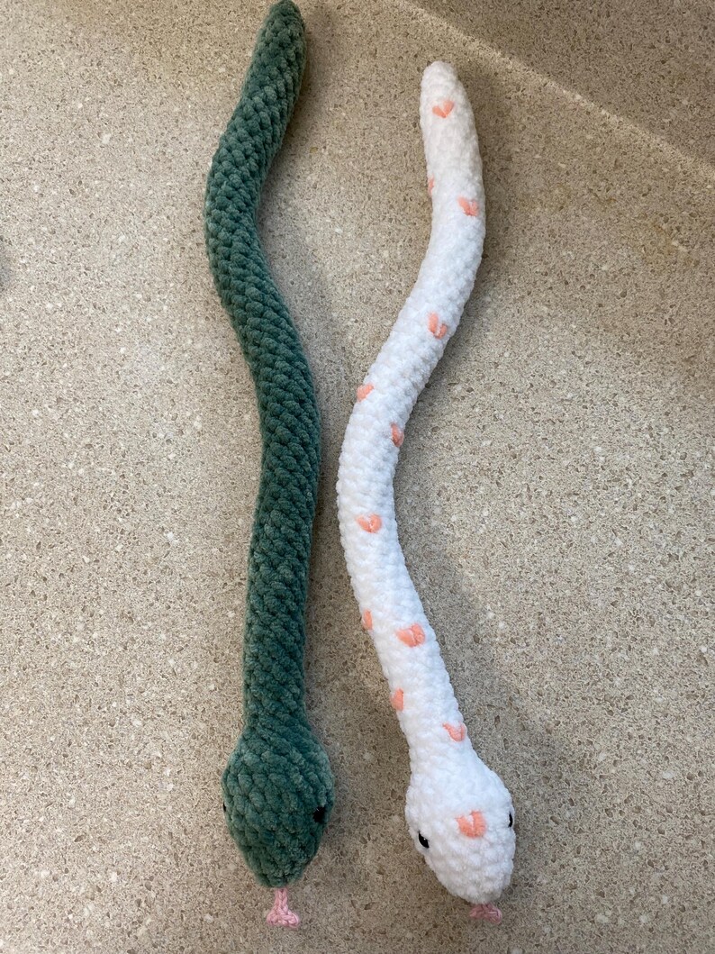 May include: Two crocheted snake toys. One is green and the other is white with pink hearts.