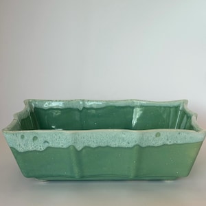 以下が含まれることがあります： 波状の縁が付いた長方形の緑色のセラミックプランター。 プランターは、テクスチャード加工された斑点のある仕上げと、より明るい緑色、ほぼ白の縁を備えています。 プランターは屋内または屋外での使用向けに設計されています。