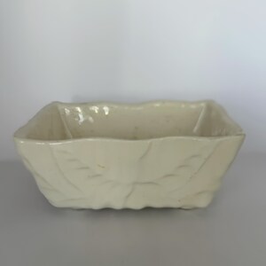 May include: Cream-colored rectangular ceramic planter with leaf imprints. The planter has a slightly textured surface and a scalloped rim. The design is simple and elegant, suitable for displaying small plants or flowers.